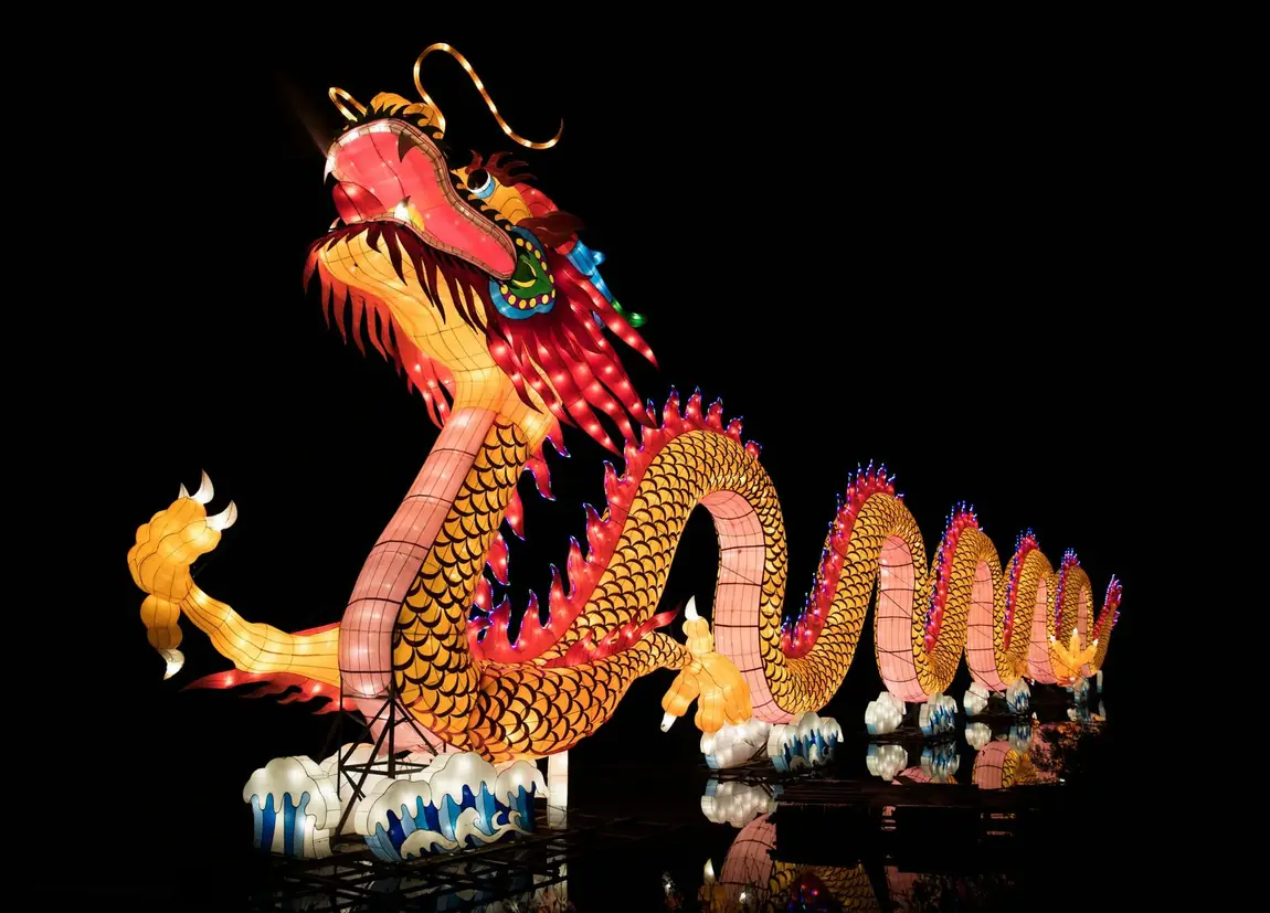 Giant Chinese dragon lantern glowing at night festival waterfront